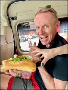 Karl holding a Banh Mi sandwich_The Big 65 Colorado Medicare Insurance Broker