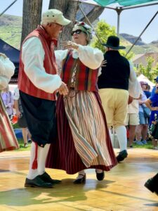 A man and lady in traditional Scandinavian dress dancing a folk dance together.