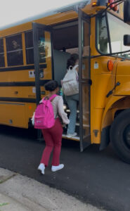 A young girl with a pink back pack getting on a school bus.