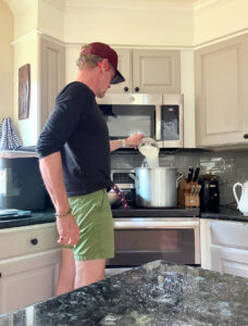 Karl pouring sugar into a large pot on a stove.