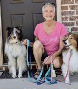 A nice lady in a pink shirt crouching between two dogs.
