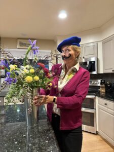 Quantz wearing a blue hat and a mustache and posting next to a flower arrangement.