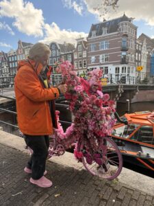 A man wearing an orange coat taking a picture of pink flowers.