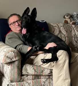 Dave with a beautiful big black dog sitting on his lap.