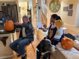 Karl carving a pumpkin as Miti and Plato watch.