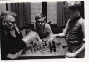 A black and white photo of Karl playing chess against his dad as a brother watches.