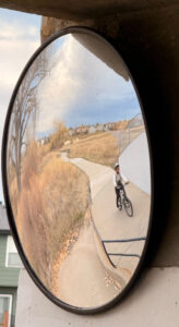 A mirror with a kid on a bike.