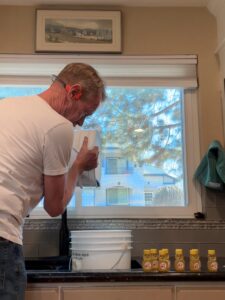 Karl in a white t-shirt holding a white pale and pouring honey.