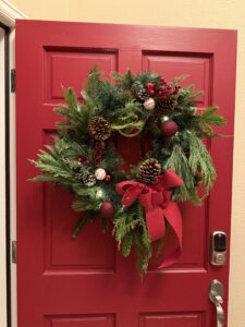 A festive Christmas wreath hanging on a bright red door.