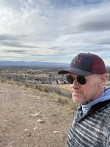 Karl wearing sunglasses and a baseball cap and looking at the Colorado vista in the distance.