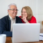 Senior couple reviewing Medicare enrollment paperwork on a laptop at home