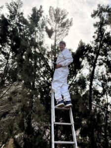 Karl in a white bee suit standing on a ladder.