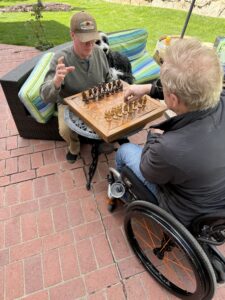 Two attractive men playing chess in the back yard.