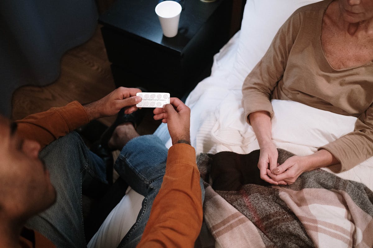 Home health caregiver discussing medication with senior patient in bed during Medicare-covered home visit