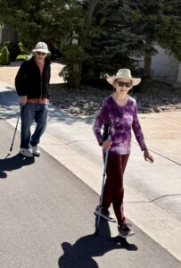 A man and a woman, both wearing hats, using walking sticks while walking.
