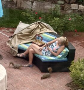 Quantz sitting on a sofa in the back yard with two squirrels at her feet.