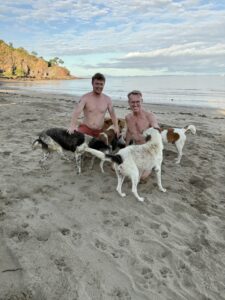 Nicholas and Karl on the beach surrounded by dogs.