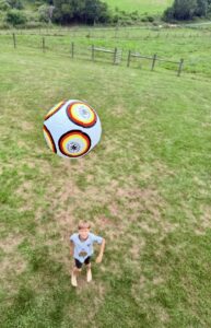 A soccer ball up in the air as a young boy looks up at the ball.