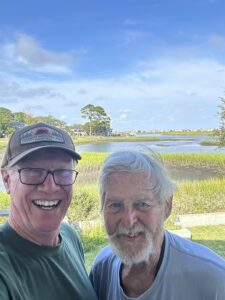 Two distinguished looking gentlemen in front of a small body of water.