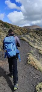 A man with a blue backpack walking on a dirt road.