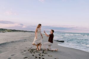 Nicholas on his knees proposing to Nicola on a beautiful beach.